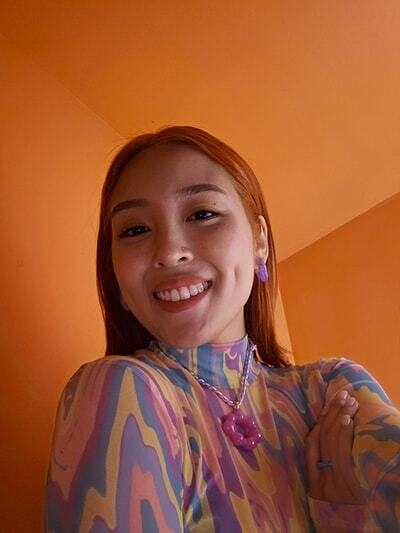 Une femme prend un selfie dans une pièce faiblement éclairée.  La lumière sur son visage est équilibrée même avec un…